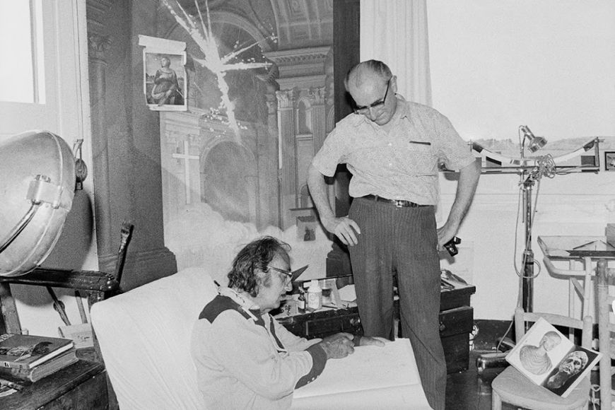 Dalí al seu taller de Portlligat, al costat del fotògraf i amic Meli. Seu davant de l'obra Explosió de fe mística amb una làmina enganxada de Santa Caterina d'Alexandria de Rafael.Foto Melitó Casals, “Meli”, 1971 | © Drets Fundació Gala - Salvador Dalí, 2022 Dalí al seu taller de Portlligat, al costat del fotògraf i amic Meli. Seu davant de l'obra Explosió de fe mística amb una làmina enganxada de Santa Caterina d'Alexandria de Rafael.Foto Melitó Casals, “Meli”, 1971 | © Drets Fundació Gala - Salvador Dalí, 2022