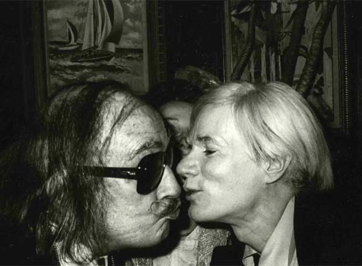 Andy Warhol fa un petó a Salvador Dalí en una fotografia de l'any 1978 a l'hotel St. Regis de Nova York. | © Christopher Makos